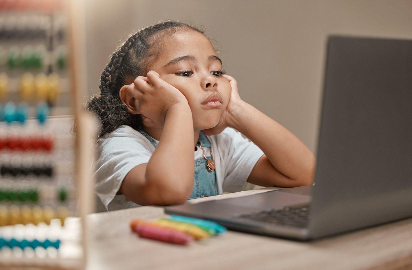 A little girl sitting at the table with her head on her hands.